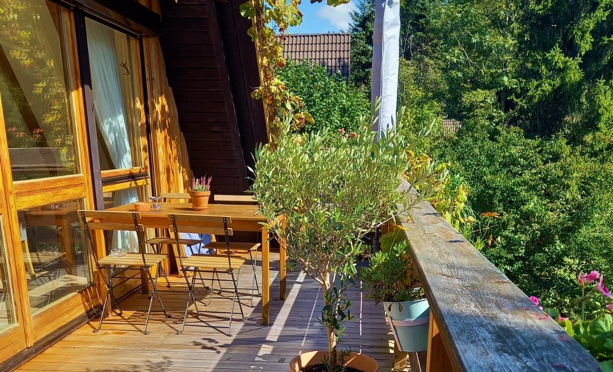 Terrasse am Ferienhaus im Chiemgau Holzterrasse mit Tisch, Stühlen und Pflanzen, umgeben von grünen Bäumen.