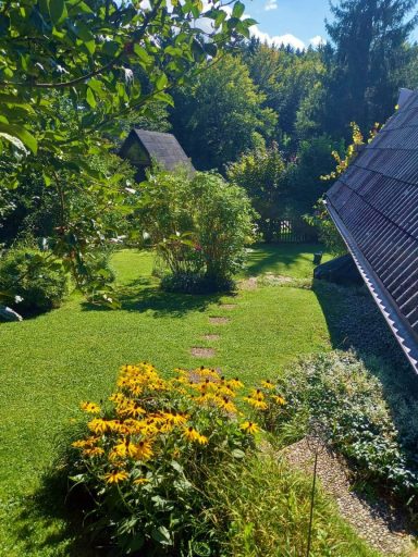 Grüner Garten mit Blumen, Wegen und Blick auf Dächer in der Ferne.
