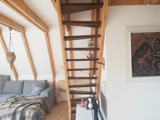 Holztreppe im Dachgeschoss, neben einem gemütlichen Sofa und einer modernen Wanddekoration.