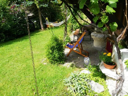 Ein sonniger Garten mit einer Liege, Pflanzen und einer Hängematte im Hintergrund.