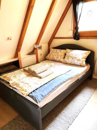 Ein gemütliches Bett mit Kissen und einer Decke in einem hellen, schrägen Raum.